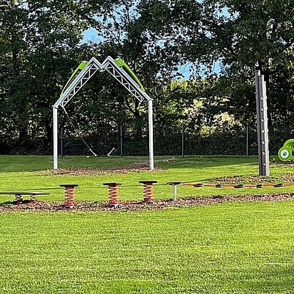 Spielplatz auf grüner Wiese mit Bäumen im Hintergrund
