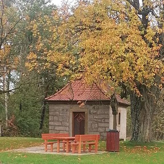 Bild des "Höfer Kapperla"; kleiner Platz mit Bäumen und einer kleinen Kapelle.